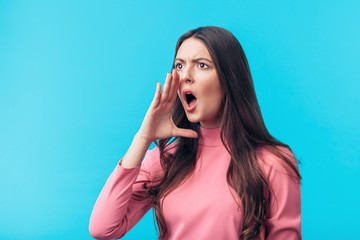 Wall Mural - Crying emotional woman screaming holding hand near mouth on blue background