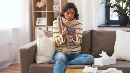 Wall Mural - health, cold and people concept - sick young woman in scarf coughing and drinking hot tea at home