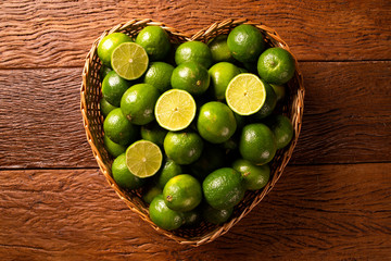 Wall Mural - Fresh limes in a heart bowl on wooden table background. Top view.