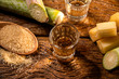 two shot glasses of Brazilian gold  cachaca with sugar and sugarcane isolated on rustic wooden background