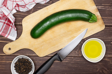 Wall Mural - One whole zucchini is ready to be chopped. recipe step by step fusilli pasta with zucchini on chopping board with a knife and a tea towel flatlay on brown wood