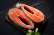 Two Raw Salmon steak on a wooden Board with salt and basil on a dark background. Fresh red fish. Healthy and diet food.