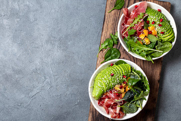 Wall Mural - Low carbs bowl. Fresh salad with green spinach, rucola, avocado an ham serrano in white bowl, gray background, top view