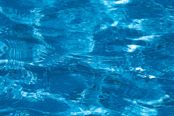 blue and bright ripple water surface in swimming pool with sun reflection.