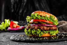 Beef Burger With Tomatoes, Red Onions, Cucumber And Lettuce On Black Slate Over Dark Background. Unhealthy Food