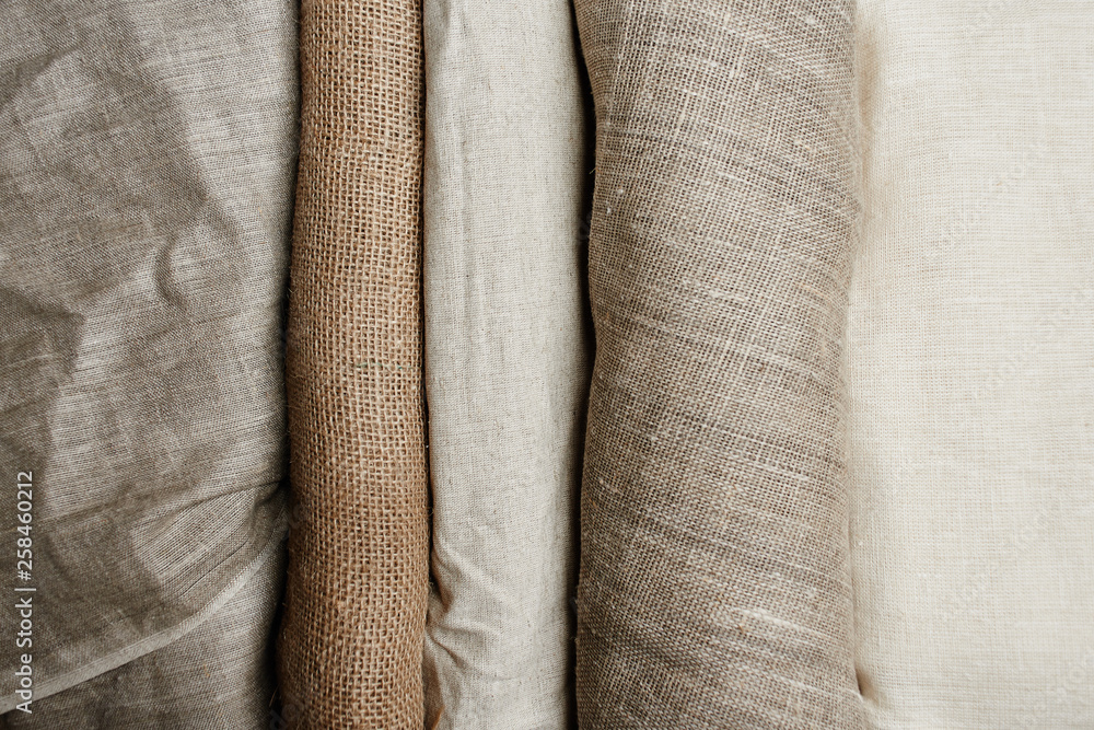 Natural fabrics from organic colors of flax and cotton in rolls, homespun textile handmade. Burlap and canvas for eco, rustic, boho, hygge decor - obrazy, fototapety, plakaty 