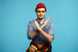 © Anatoliy Karlyuk - No work for today. Body language, signs, symbols and gestures. Isolated picture of positive young foreman wearing protective goggles, red hat and tool belt making stop gesture, crossing his hands
