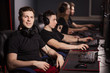 © alfa27 - Satisfied smart gamer in black t-shirt sitting behind the computer monitor and looking at camera in a gaming club or internet cafe with the other people playing.