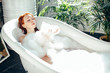 Playful young caucasian woman enjoying foam bath at home. Resting, relaxing, blowing on a cloud of foam