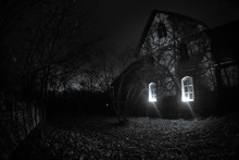 Old House With A Ghost In The Forest At Night Or Abandoned Haunted Horror House In Fog. Old Mystic Building In Dead Tree Forest. Trees At Night With Moon.