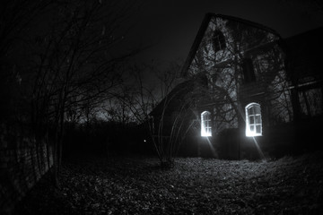 Old house with a Ghost in the forest at night or Abandoned Haunted Horror House in fog. Old mystic building in dead tree forest. Trees at night with moon.