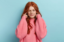 Young Lovely Ginger Female Musician Plugs Ears As Hears Awful Noise Or Music, Squints Face, Has Long Wavy Foxy Hair, Wears Oversized Pink Jumper, Avoids Loud Sound, Ignores Something Unpleasant