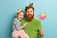 Happy Ginger Family Of Father And Daughter Wear Party Accessories, Hold Striped Toy Windmill, Celebrate Fathers Day Or Birthday, Isolated Over Blue Background. Fatherhood And Celebration Concept