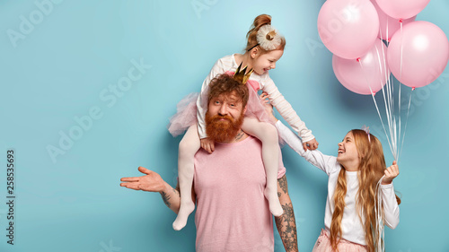 Photo of uncertain dad celebrates birthday party with daughters, can not understand how to amuse children. Happy small sisters play during balloon theme party. Family and entertainment concept
