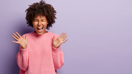 Wall Mural - Image of emotional joyful Afro American woman spreads palms, has mouth wide opened, exclaims emotionaly, wears knitted jumper, glad to be promoted at work, has bushy black hair, poses indoor