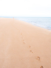 Footprints On A Tropical Beach, Fading Towards Horizon, With A Woman Far Away
