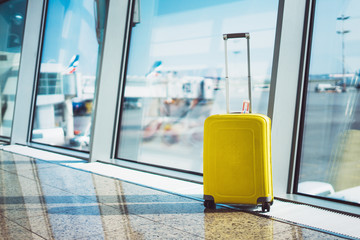 isolate traveler tourist yellow suitcase at floor airport on background large window, luggage waiting in departure area hall of ​airport lobby terminal, vacation trip concept, empty space mockup