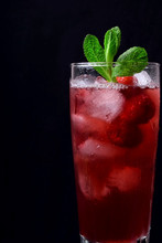 Red Drink With Ice, Raspberries And Mint In A Tall Glass Against The Black Background