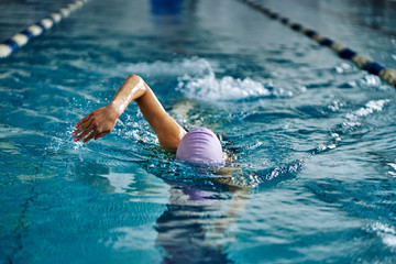 Female athlete swimming fast in crawl style.  Splashes of water scatter in different directions.