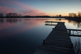 Fototapeta Pomosty - Wooden jetty on a calm lake and pink clouds after sunset