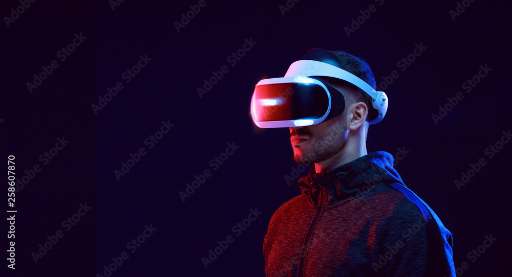 Model young man with beard in glasses of virtual reality on dark background.. Augmented reality, science, future technology concept. VR. Futuristic 3d glasses with virtual projection. Neon light. - obrazy, fototapety, plakaty 