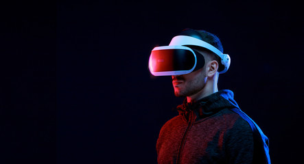 Model young man with beard in glasses of virtual reality on dark background.. Augmented reality, science, future technology concept. VR. Futuristic 3d glasses with virtual projection. Neon light.
