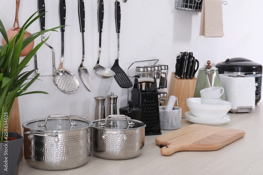 Set of clean cookware, dishes, utensils and appliances on table at white wall - obrazy, fototapety, plakaty 