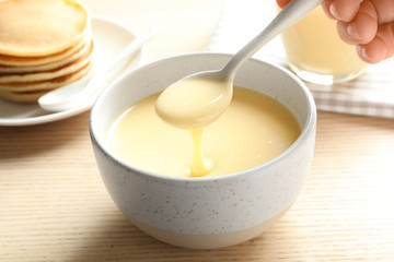 person holding spoon with condensed milk over bowl on table, closeup. dairy products