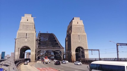 Poster - Fast traffic entering the Sydney harbour bridge on a sunny day across multi lanes with bus lane and divided traffic under massive steel arch.