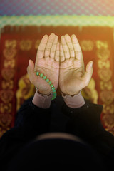 Close view of muslim woman praying to Allah with hands up on praying mat, holding beads