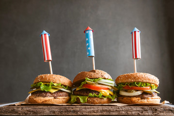 Wall Mural - three fresh and juicy burgers with American flag-style fireworks inserted into them. bbq concept picnic to celebrate independence day