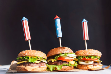 Wall Mural - three fresh and juicy burgers with American flag-style fireworks inserted into them. bbq concept picnic to celebrate independence day