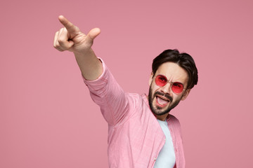 Portrait of a happy cheerful hipster male in pink shirt pointing finger at camera, screaming and standing over pink background. Lucky man acts like he won something with copys space.