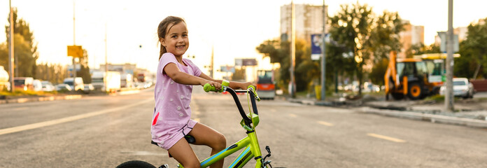 Wall Mural - Children learning to drive a bicycle on a driveway outside. Little girls riding bikes on asphalt road in the city wearing helmets as protective gear.