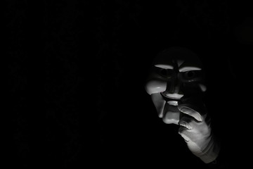 White scary mask on a black background with whites hand.