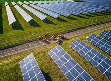 Solar Panel Produces Green, Environmentaly Friendly Energy From The Setting Sun. Aerial View From Drone. Landscape Picture Of A Solar Plant That Is Located Inside A Valley With Sheep