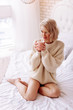© zinkevych - Young woman wearing beige sweater holding cup with hot tea