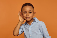 Overhear, Spy And Secrecy Concept. Isolated Studio Portrait Of Cute Nosy African Ten Year Old Boy Spying On Someone, Keeping Hand At His Ear And Listening Attentively, Trying To Hear Everything