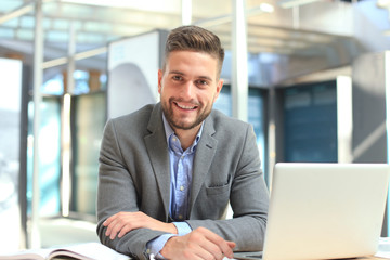 portrait of happy businessman sitting at office desk, looking at camera, smiling.