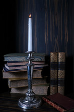 An Old Silver Candlestick With A Burning Candle On The Background Of Old Books.