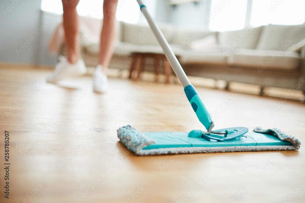 Close-up of unrecognizable woman using mop with microfiber pad while cleaning parquet floor in living room - obrazy, fototapety, plakaty 