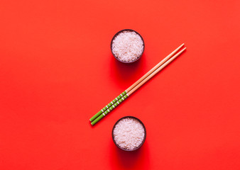 Wall Mural - Uncooked rice in bowls with chopsticks on coral background. Trendy color 2019. 