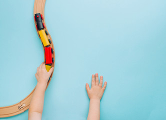 Wall Mural - Kids hands playing with wooden toy train on blue background