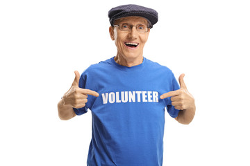 Poster - Cheerful elderly man wearing a volunteer signed t-shirt and pointing at it