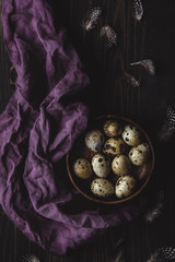 Wall Mural - Quail eggs in wooden bowl with feathers on dark wooden background.