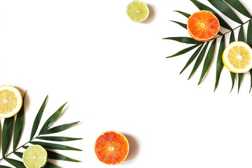 Exotic composition of fresh lemons, red oranges, lime fruit and lush green palm leaves isolated on white table background. Tropical summer vacation concept. Flat lay, top view. Decorative frame.