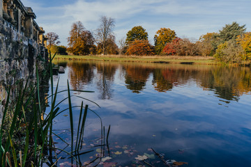 Beautiful autumn garden with tree reflections in water, old stone wall. Hever Castle Gardens, Kent, England.