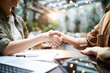 © Seventyfour - Close-up of unrecognizable business partners sitting at table with papers and laptop and shaking hands after concluding deal in cafe