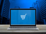 Fototapeta Panele - Shopping cart flat icon with modern laptop computer on wooden table over office city tower and skyscraper, Business shop online concept