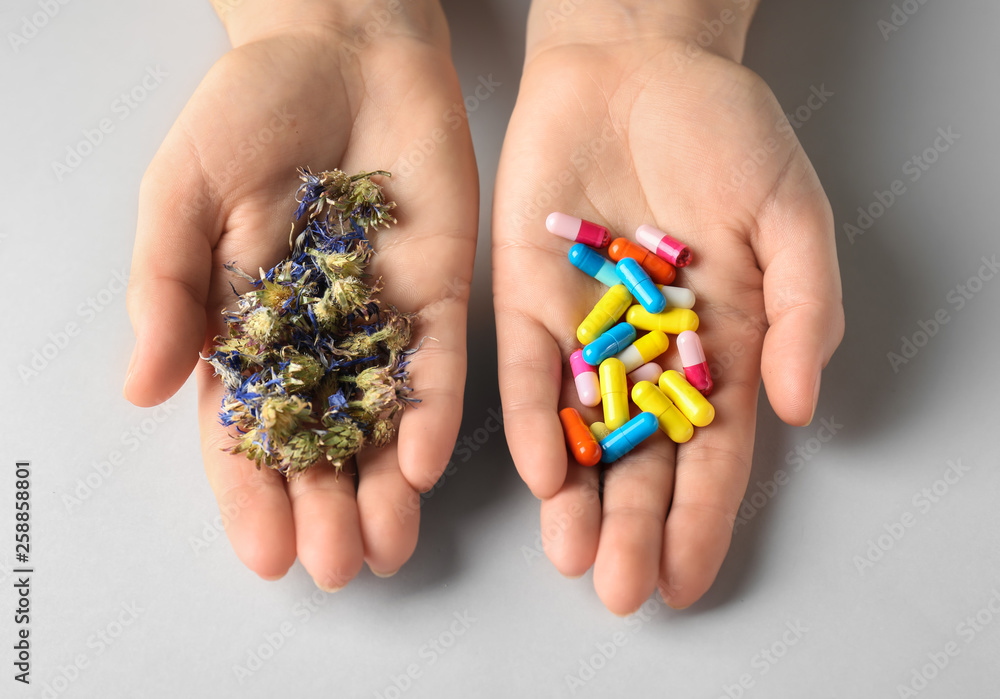 Female hands with plant based pills and dry flowers on white background